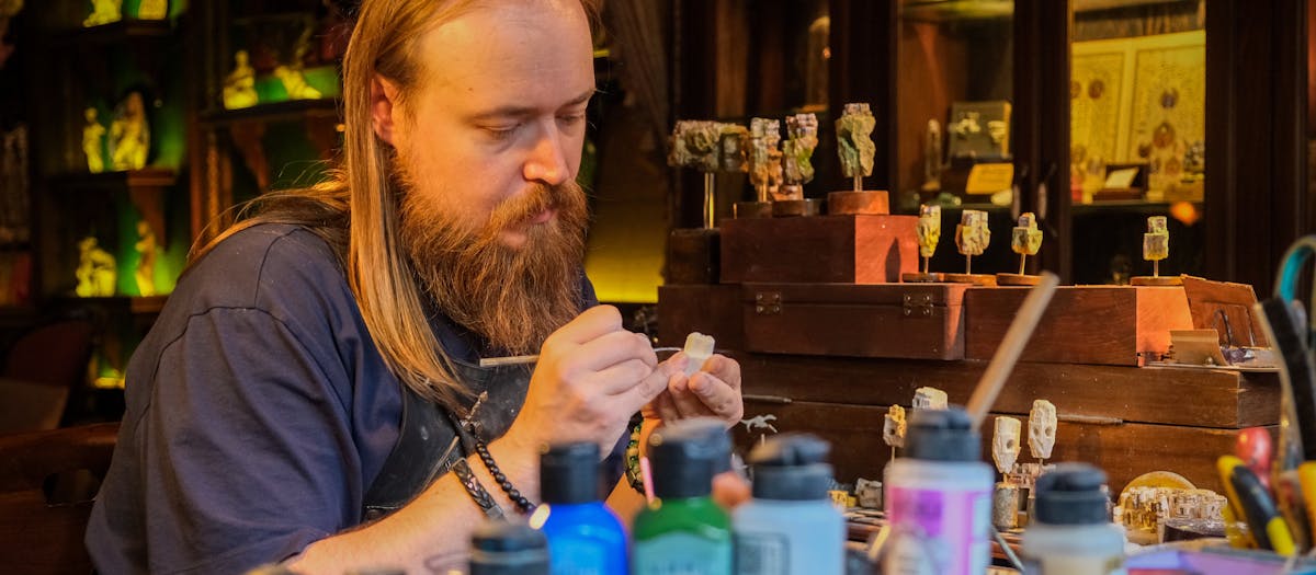 Skilled artisan meticulously painting miniatures in a cozy, cluttered workshop with various vibrant paints.